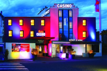 Façade illuminée du Casino de Plouescat la nuit, mettant en valeur son architecture moderne au bord de la mer.
